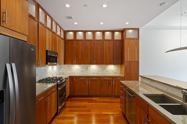 kitchen with sink, hardwood / wood-style flooring, appliances with stainless steel finishes, light stone counters, and decorative backsplash