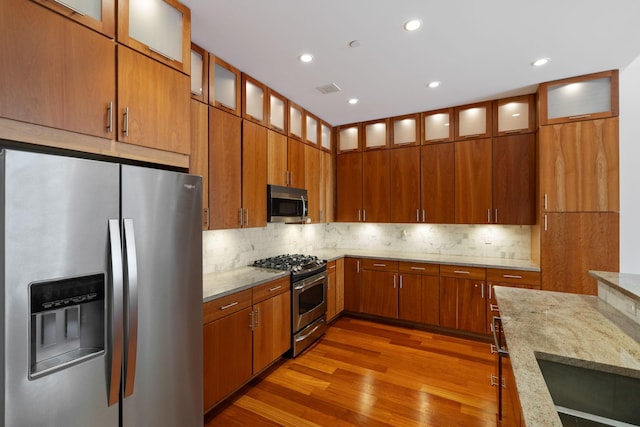 kitchen with stainless steel appliances, hardwood / wood-style floors, backsplash, and light stone counters