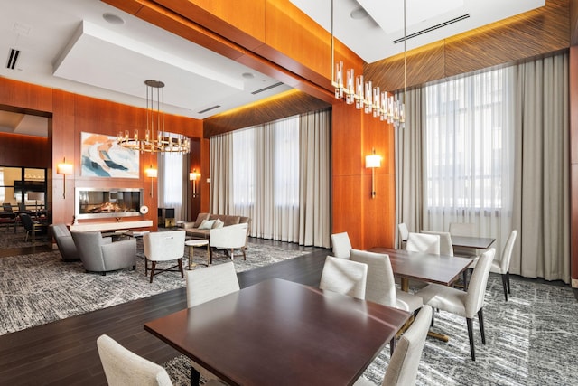 dining area with wooden walls, a tray ceiling, a chandelier, and dark hardwood / wood-style flooring