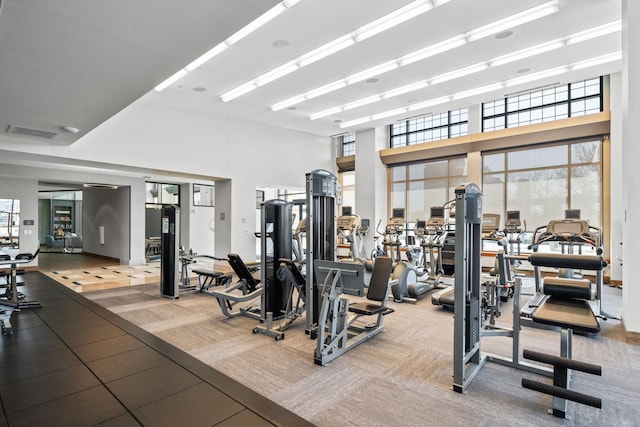 gym with light carpet, plenty of natural light, and a high ceiling