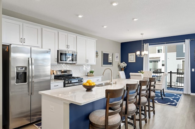 kitchen featuring stainless steel appliances, tasteful backsplash, a sink, an island with sink, and light wood-type flooring