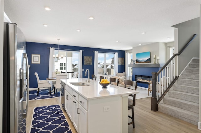 kitchen featuring stainless steel fridge, white cabinets, a glass covered fireplace, light wood-type flooring, and a sink