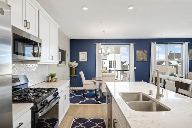 kitchen featuring stainless steel appliances, light wood-style flooring, decorative backsplash, white cabinetry, and a sink