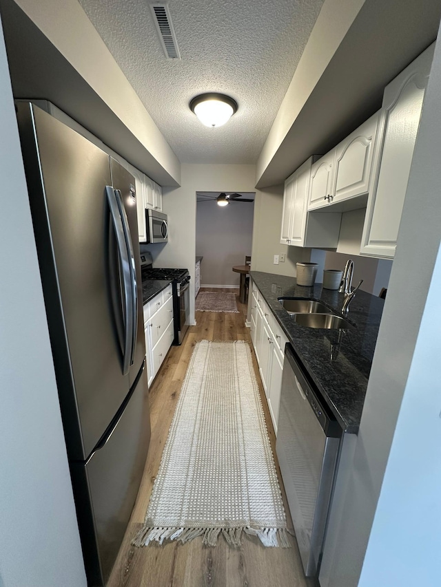 kitchen with white cabinetry, sink, dark stone countertops, stainless steel appliances, and light wood-type flooring