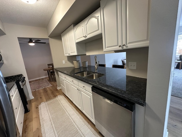 kitchen with sink, white cabinetry, stainless steel dishwasher, dark stone counters, and light wood-type flooring