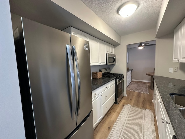 kitchen featuring light hardwood / wood-style flooring, appliances with stainless steel finishes, white cabinetry, dark stone countertops, and a textured ceiling