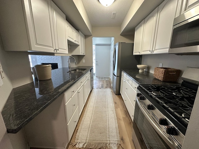 kitchen featuring sink, white cabinetry, light hardwood / wood-style flooring, dark stone countertops, and appliances with stainless steel finishes