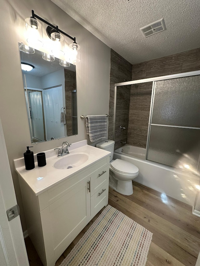 full bathroom featuring combined bath / shower with glass door, vanity, wood-type flooring, a textured ceiling, and toilet