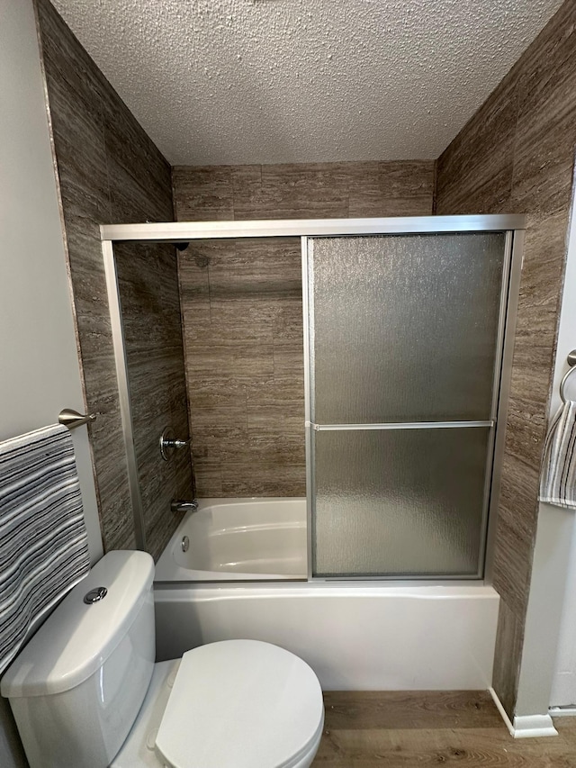 bathroom with toilet, combined bath / shower with glass door, and a textured ceiling