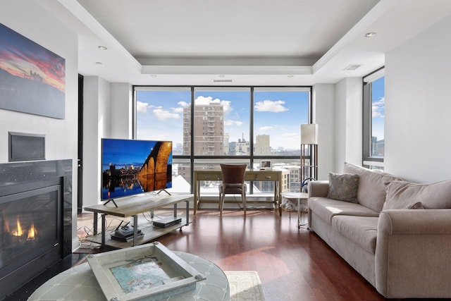 living room with dark hardwood / wood-style flooring, a wall of windows, and a raised ceiling