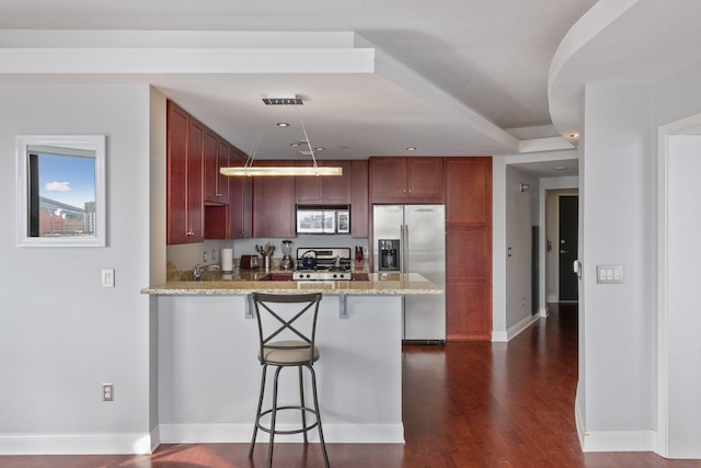 kitchen with dark wood-type flooring, a breakfast bar area, kitchen peninsula, stainless steel appliances, and light stone countertops