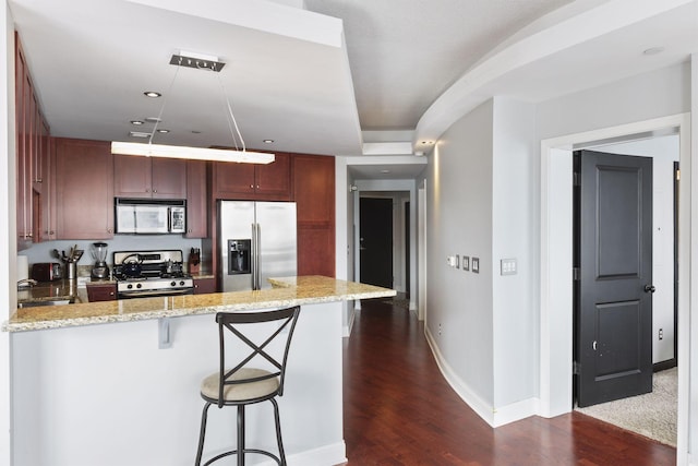 kitchen with appliances with stainless steel finishes, a breakfast bar, dark hardwood / wood-style floors, kitchen peninsula, and light stone countertops