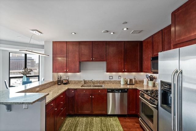 kitchen featuring sink, appliances with stainless steel finishes, light stone countertops, a kitchen bar, and kitchen peninsula