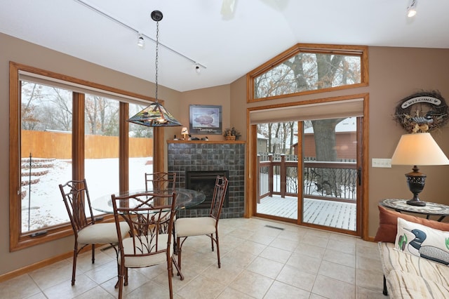 tiled dining area featuring vaulted ceiling, rail lighting, and a fireplace