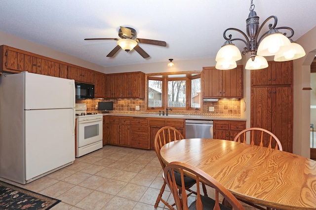 kitchen with sink, tasteful backsplash, hanging light fixtures, white appliances, and ceiling fan with notable chandelier