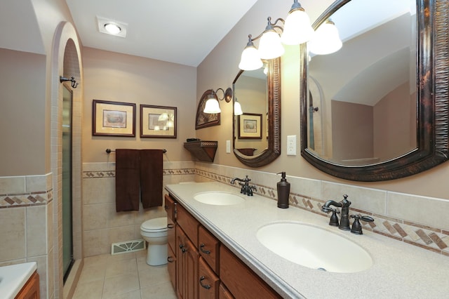 bathroom featuring a shower with shower door, tile walls, tile patterned flooring, vanity, and toilet