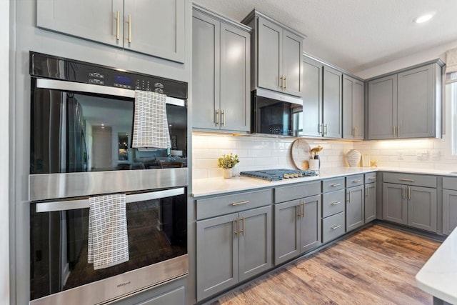 kitchen with tasteful backsplash, gray cabinets, stainless steel appliances, and wood finished floors