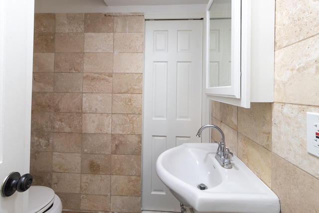 half bath featuring a sink, toilet, and tile walls