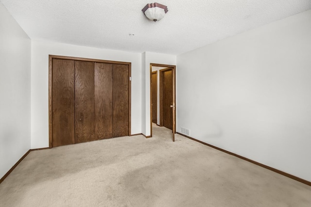 unfurnished bedroom with a closet, light colored carpet, a textured ceiling, and baseboards