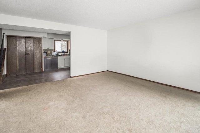 unfurnished living room featuring a textured ceiling, dark colored carpet, and baseboards