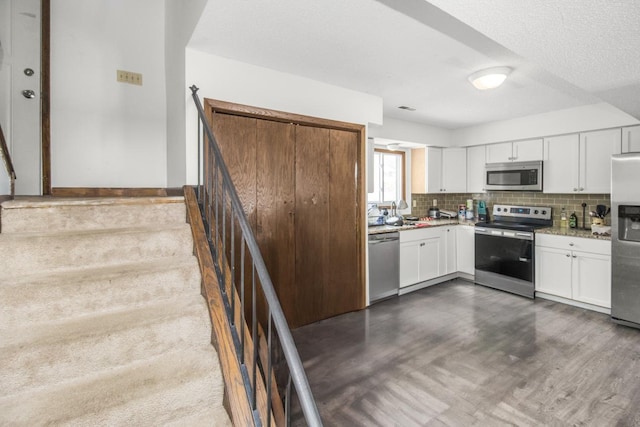 kitchen featuring light stone counters, stainless steel appliances, white cabinetry, backsplash, and dark wood finished floors