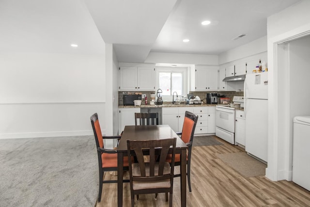 kitchen with white appliances, visible vents, under cabinet range hood, white cabinetry, and backsplash