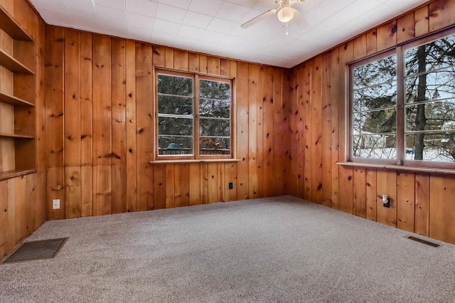 spare room featuring ceiling fan, wooden walls, and carpet