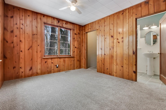 spare room featuring sink, light colored carpet, ceiling fan, and wood walls