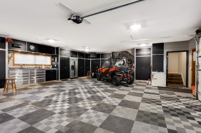 garage with a garage door opener and stainless steel refrigerator with ice dispenser