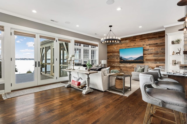 living room featuring dark wood-type flooring, ornamental molding, wood walls, and a water view