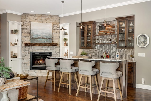 bar featuring dark wood-type flooring, crown molding, pendant lighting, a fireplace, and light stone countertops