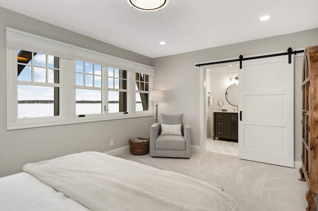 bedroom featuring connected bathroom, light colored carpet, and a barn door