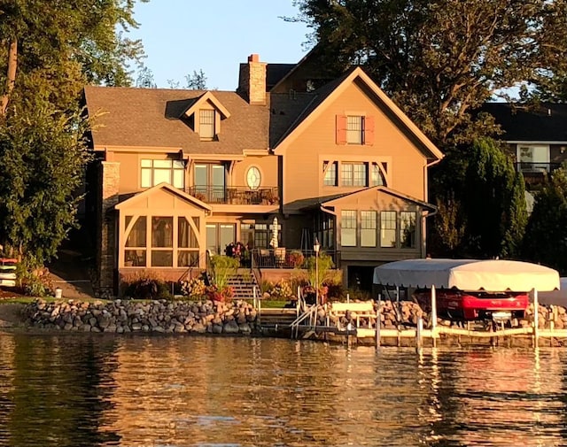 rear view of property featuring a sunroom, a balcony, and a water view