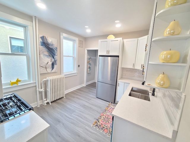 kitchen featuring radiator, stainless steel refrigerator, sink, white cabinets, and light stone counters