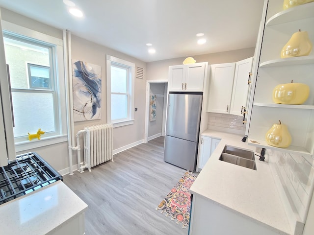 kitchen featuring sink, white cabinetry, tasteful backsplash, stainless steel fridge, and radiator