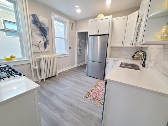 kitchen featuring sink, stainless steel refrigerator, radiator heating unit, decorative backsplash, and white cabinets