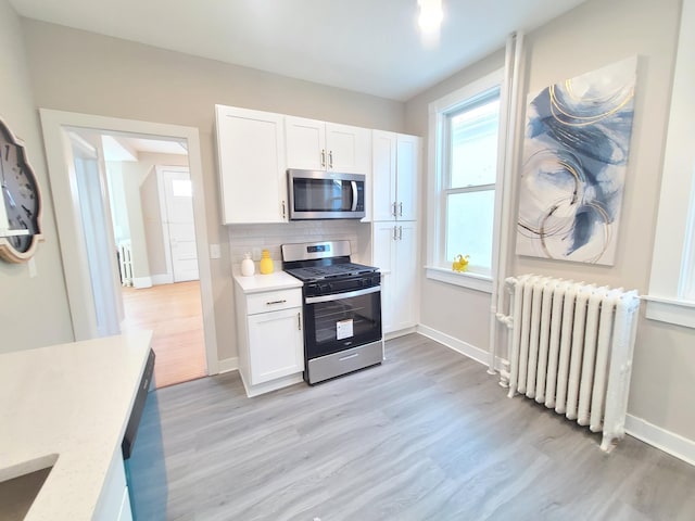 kitchen with appliances with stainless steel finishes, radiator heating unit, white cabinets, backsplash, and light wood-type flooring