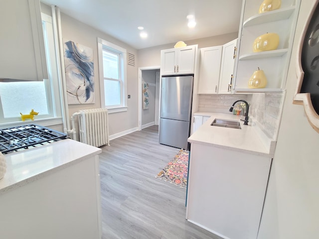 kitchen with radiator, sink, stainless steel refrigerator, white cabinetry, and backsplash