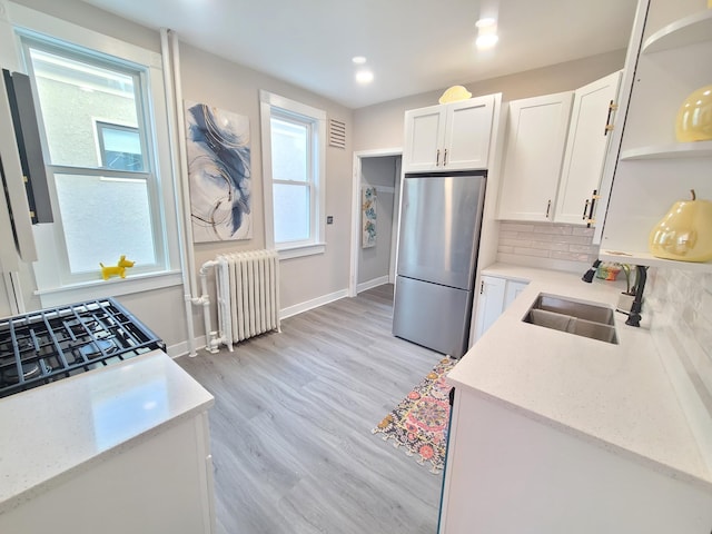 kitchen with sink, stainless steel refrigerator, radiator heating unit, decorative backsplash, and white cabinets