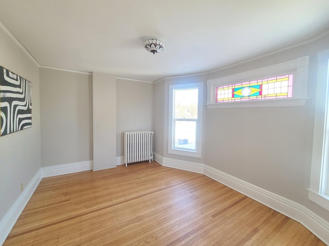 empty room featuring ornamental molding, radiator heating unit, and light wood-type flooring