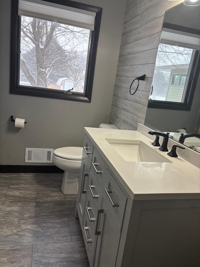 bathroom with wood walls, vanity, toilet, and plenty of natural light