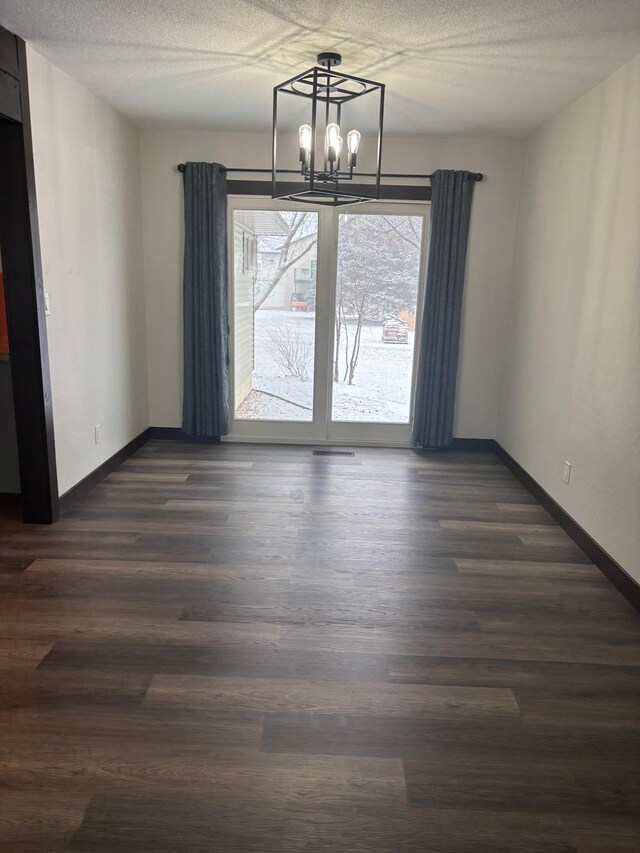 unfurnished dining area featuring dark hardwood / wood-style flooring, a notable chandelier, and a textured ceiling