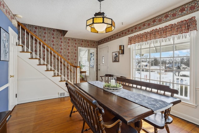 dining area featuring wallpapered walls, baseboards, stairway, wood finished floors, and a textured ceiling