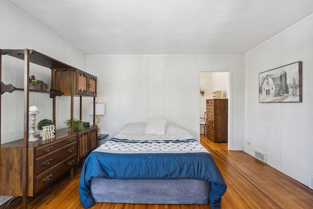 bedroom with ornamental molding, visible vents, and wood finished floors