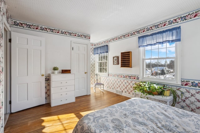 bedroom with wood finished floors, visible vents, baseboards, and wallpapered walls