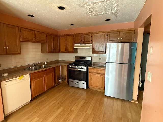 kitchen with appliances with stainless steel finishes, sink, decorative backsplash, light hardwood / wood-style floors, and a textured ceiling