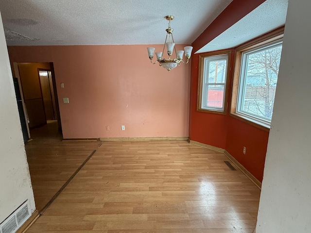 unfurnished room featuring a notable chandelier, light hardwood / wood-style flooring, and a textured ceiling