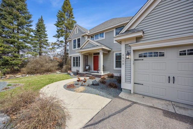 traditional-style house featuring an attached garage, driveway, a front lawn, and roof with shingles