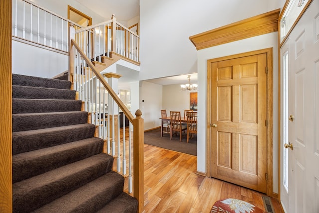 foyer featuring stairway, light wood finished floors, a towering ceiling, an inviting chandelier, and baseboards