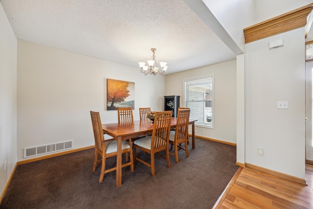 dining room featuring a textured ceiling, wood finished floors, an inviting chandelier, baseboards, and visible vents